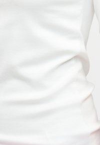 Κοντινό πλάνο λευκού υφασμάτινου ενδύματος που δείχνει απαλές πτυχές και ελαφρά τέντωμα στη μία πλευρά.