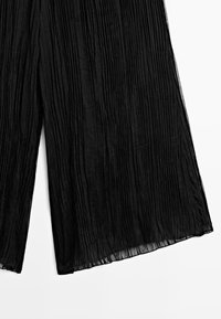 Black pleated wide-leg pants made of light, textured fabric. Features vertical pleats, a flowing design, and a hemline with a sheer finish.