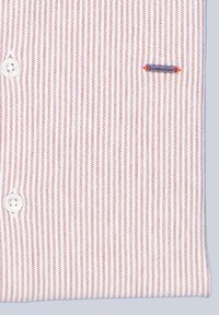 Weißes Hemd mit Knöpfen, das schmale rote vertikale Streifen aufweist, eine glatte Textur hat und ein kleines, unauffälliges Logo auf der linken Brust trägt.