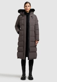 Lange, gewatteerde jas in donkergrijs met een faux bont-trimmed capuchon, met een rits aan de voorkant en twee zijzakken. Gekozen boven zwarte kleding.