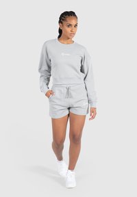 Lys grå cropped sweatshirt med lange ærmer og ribbede manchetter, parret med matchende shorts med snøre. Hvid logo detalje på begge dele.