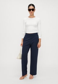 Bílý žebrovaný dlouhý rukáv crop top, námořnické široké kalhoty s bočními švy, hnědé sandály na pásku a malá béžová kabelka.