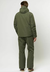 Olíva zöld szigetelt dzseki kapucnival, hozzá illő nadrággal párosítva. Simává textúrája, egyenes vonalvezetése és könnyű anyaga van.