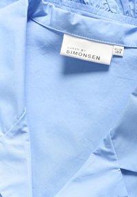 Tessuto blu chiaro con una superficie liscia, dotato di un colletto e di un'etichetta con la scritta "KAREN BY SIMONSEN", taglia EU 38 e taglia US 8.