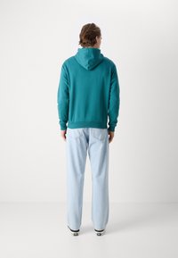 Teal hoodie with a kangaroo pocket and adjustable drawstring. Paired with light blue wide-leg jeans and black canvas sneakers.