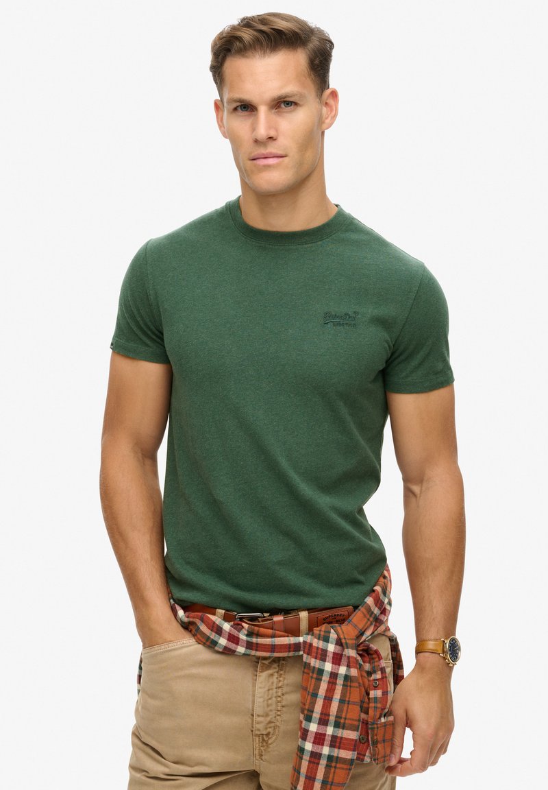 Groen katoenen T-shirt met korte mouwen en een ronde hals. Kenmerkt zich door een subtiele logo op de borst, gecombineerd met een geruite shirt dat om de taille is geknoopt.