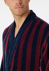 Bata de baño a rayas con una combinación de colores en azul marino oscuro y burdeos, hecha de un tejido suave con cuello de solapa y un acabado texturizado.