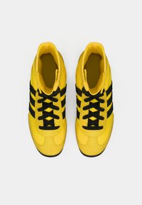 Yellow athletic shoes with black stripes. Features include laces, rounded toe, and a textured sole. Made of synthetic material.