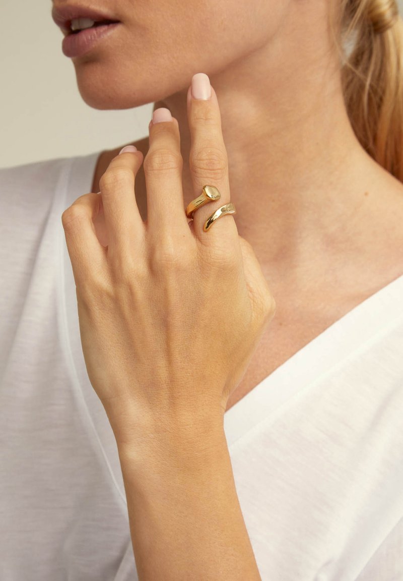 Anillos apilables de oro con un acabado suave y pulido. Un anillo presenta una forma redondeada y el otro tiene un diseño texturizado e irregular.