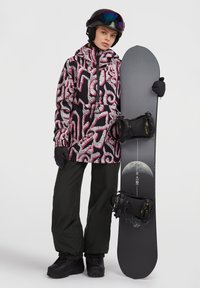 Snowboarder in een gestreepte zwart en roze jas, zwarte handschoenen en donkergroene broek, die een zwarte snowboard met bindingen vasthoudt.