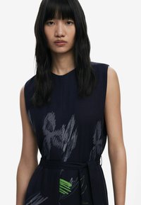 Navy sleeveless dress with a textured pattern featuring gray and green brushstroke designs; includes a tied waist and a v-neckline.