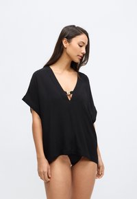 Črni, lahko zgornji del z globokim V-izrezom in kratkimi rokavi. Ima kovinski zaponko na izrezu in ohlapno, sproščeno prileganje.