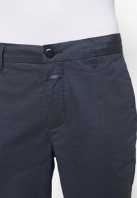 Mörkblå bomullsbyxor med en slät yta, med en framficka, knappstängning och en logotagg på sidan.