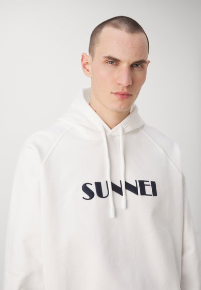 Hoodie bianco realizzato in tessuto morbido, con tasca a canguro e cordini. La parte anteriore presenta un logo ricamato "SUNNEI" in blu navy.