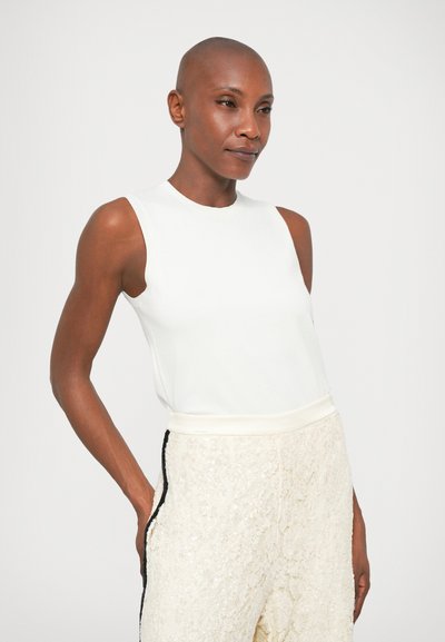 Top branco sem mangas com decote redondo. Combinado com calças texturizadas de cor clara com uma risca preta na lateral. Tecido suave.