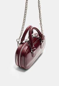 Borsa in pelle borgogna con finitura lucida, forma arrotondata e doppi manici. Presenta una tracolla in catena argentata e chiusura con zip superiore.