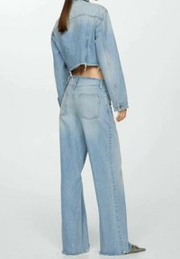 Chaqueta de mezclilla azul claro con diseño corto y dobladillo deshilachado, combinada con jeans de talle alto y pierna ancha que cuentan con bolsillos traseros.