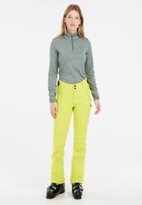 Grijze lange mouwen zip-pullover gecombineerd met felgele hoge skibroek, met twee voorzakken en knoopsluiting bij de taille.
