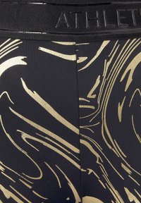 Black leggings with a shiny gold swirled pattern, featuring a textured elastic waistband labeled "ATHLETE." Smooth fabric with a matte finish.
