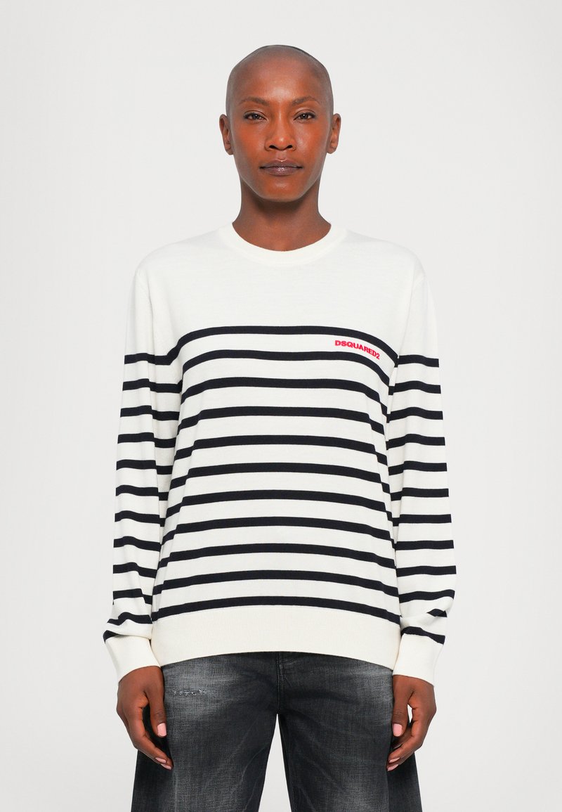 Person with shaved head wearing white and black horizontal striped sweater with red "DSQUARED2" logo, paired with dark washed jeans.