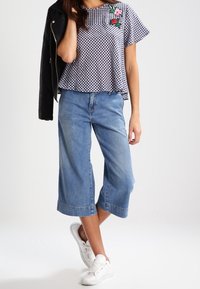 Svart och vit rutigt kortärmad topp med blommönster, parat med ljusblå vida denimculotter och vita sneakers.