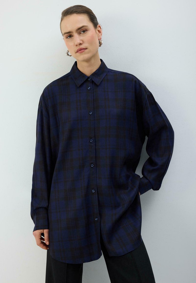 Marineblå ternet skjorte med lange ærmer, spids krave og knaplukning. Stoffet virker blødt med en afslappet, oversized pasform.