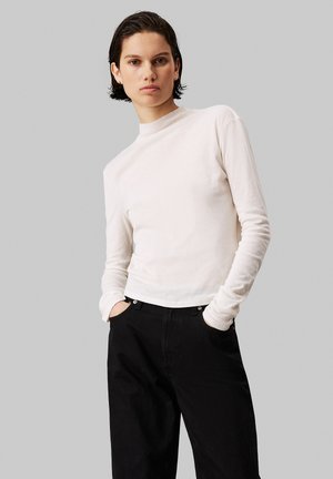 Crème lange mouw top met hoge hals en een lichte, gladde textuur, gecombineerd met hoge zwarte jeans met voorzakken.
