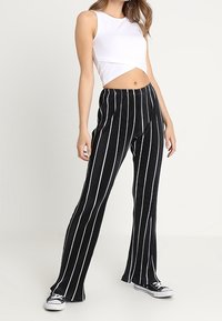 Pantaloni a gamba larga a righe bianche e nere con texture a coste, abbinati a un crop top fitted bianco e sneaker nere.