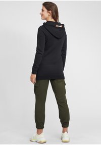 Felpa nera con finitura testurizzata, dotata di cappuccio con coulisse e accento in pelle marrone. Abbinata a pantaloni cargo verdi oliva.