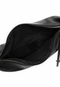 Pochette en cuir noir avec une texture lisse, fermeture zippée et un intérieur doublé comportant un petit compartiment zippé. Étiquette de logo visible à l'intérieur.