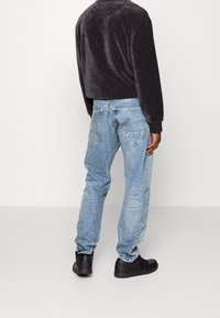 Svart kordjaket med kort längd och ribbade ärmslut, kombinerat med ljust tvättade raka jeans. Modellen bär svarta sneakers och visas från ryggen.