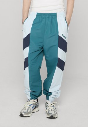 Turkise og lyseblå treningsbukser med marineblå aksenter, elastisk midje, sidelommer og ribbestrikkede mansjetter. Har et karakteristisk chevronmønster.