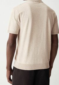 Polo en tricot beige à manches courtes avec col et ourlet côtelés, présentant une texture lisse et une coupe ajustée, vu de dos.