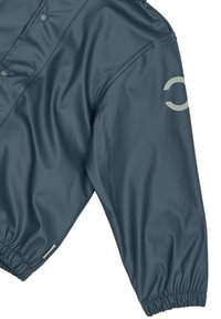 Sötétkék szélálló dzseki sima, fényes felülettel. A vállán világosszürke, ívelt logó található, a rugalmas mandzsetták pedig kényelmes, szoros illeszkedést biztosítanak.