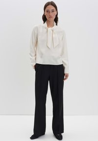 Blusa bianca con cravatta al collo, maniche lunghe, morbida al tatto; abbinata a pantaloni neri a vita alta, con un design a gamba dritta.