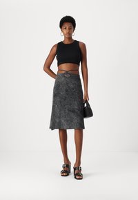 Fekete crop top, szürke textúrájú midi szoknyával párosítva, amelynek egyedi fűzött derék részlete van. A modellen fekete szandál és egy kicsi táska található.
