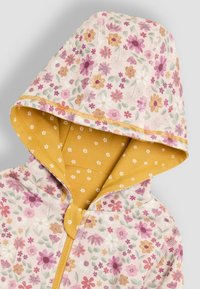 Giacca con cappuccio a fantasia floreale, caratterizzata da un tessuto esterno rosa con fiori multicolore e una fodera gialla a pois.