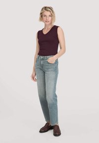 Bordeaux-farbenes ärmelloses Top, kombiniert mit hellblauen geraden Jeans und abgerundet mit kastanienbraunen Slippern. Einfaches Design und lässige Passform.