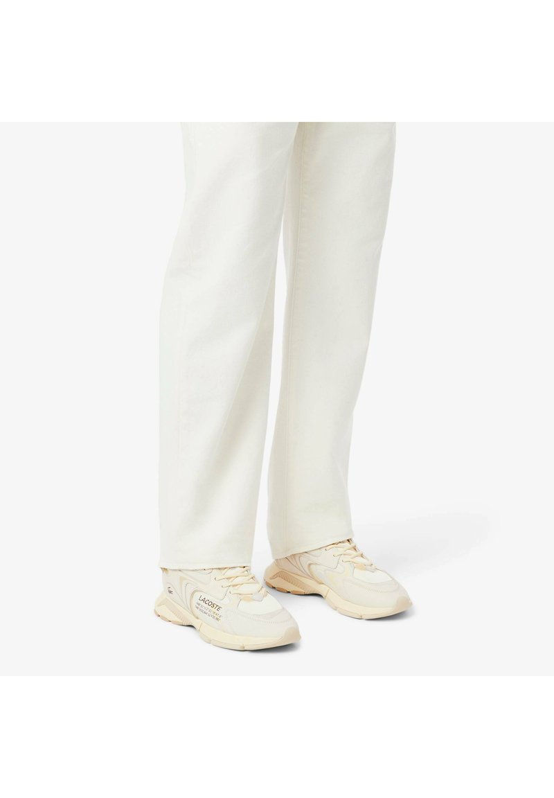 Lichtbeige sneakers met geperforeerde meshpanelen en rubberen zolen, voorzien van subtiele branding aan de zijkant, gecombineerd met witte wijde broek.