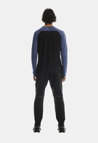 Mustmust mustrinda pikka varrukaga spordipaita musta ja sinise värviga, mis on veidi lõdva istuvusega, koos mustade pükstega. Pükstel on peegeldavad aktsendid.