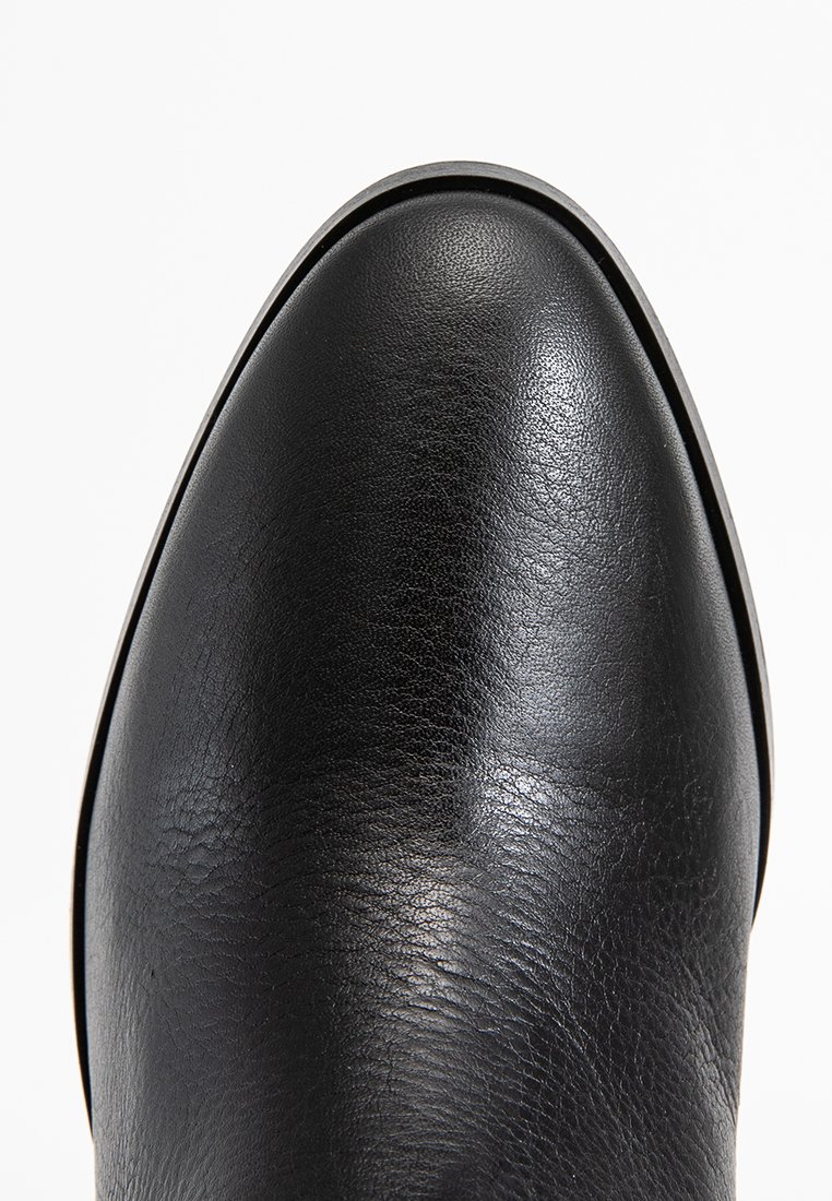 Bottine en cuir noir avec un bout arrondi, texture lisse, subtil éclat et design minimaliste. Aucune quincaillerie ou motif visible.