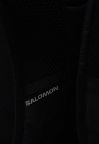Zwarte mesh en stof rugzakinterieur met het label "Salomon" in zilver. Bevat zowel gladde als gestructureerde secties, die duurzaamheid en ontwerp uitstralen.
