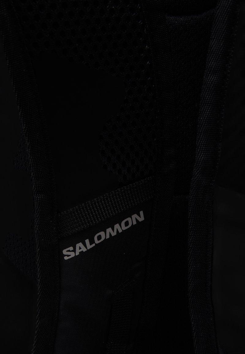 Interno di uno zaino in rete nera e tessuto con etichetta "Salomon" in argento. Presenta sezioni lisce e texturizzate, evidenziando la robustezza e il design.