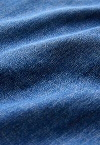 Nahaufnahme von blauer Denim-Stoff, die Textur und Falten mit sichtbarem Gewebe-Muster und Farbvariationen zeigt.