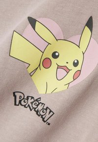 Tessuto rosa chiaro con un grande grafico di Pikachu giallo, sullo sfondo di cuori rosa e il testo nero "Pokémon" in basso.