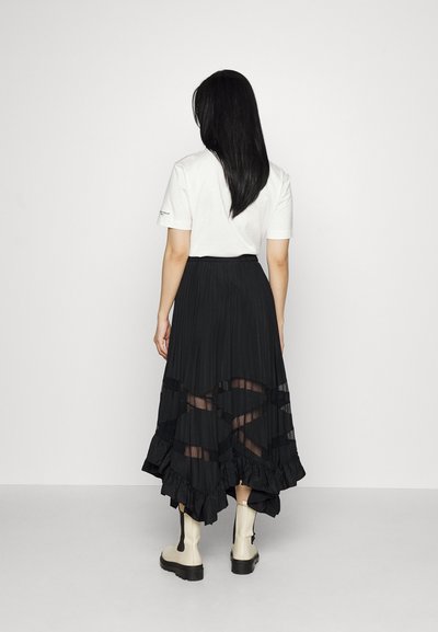Zwarte geplooide rok met gelaagde ruffles, doorzichtige inzetpatronen, elastische tailleband, gecombineerd met een witte t-shirt en beige enkelboots.