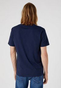 Camiseta de algodón azul marino con mangas cortas, cuello redondo y un corte relajado. La vista trasera muestra una textura suave y un diseño minimalista.