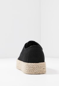 Chaussure espadrille noire avec une semelle en jute tressé. La tige présente un tissu texturé, avec une silhouette basse et sans aucune marque visible.