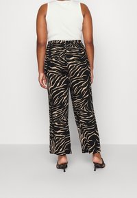 Zebra print wijde broek in zwart en tan met een elastische tailleband, gemaakt van stof met een gladde textuur en een lichte drapering.