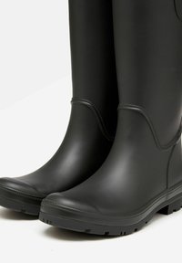 Črne gumijaste škornje imajo gladko mat površino, zaobljene prste in teksturirane podplate za dober oprijem. Opozorna šivana ob robovih dodaja detajle.